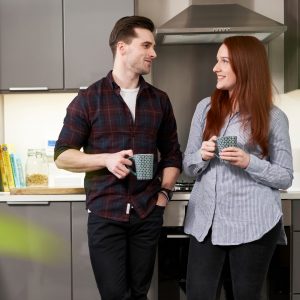 Two people smiling and holding mugs in a kitchen setting.